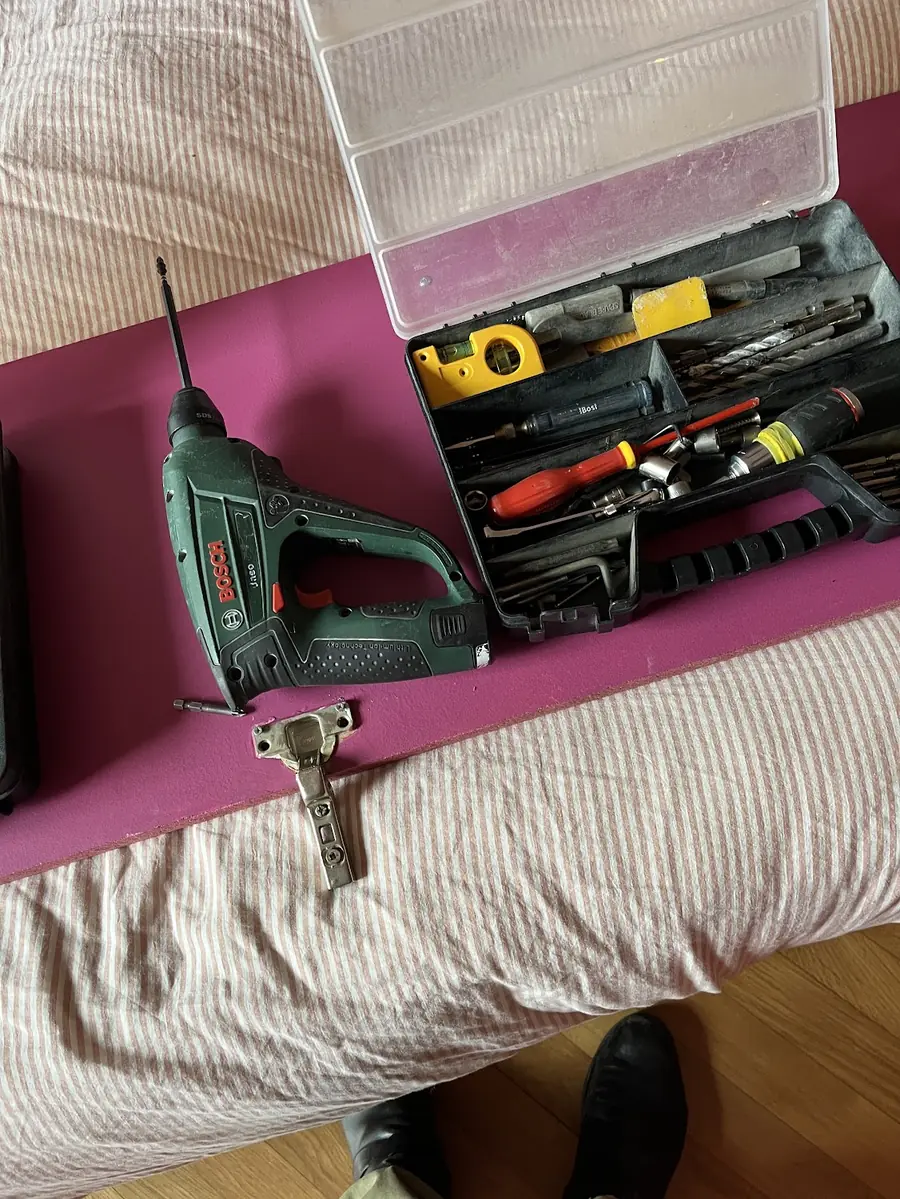 Caisse à outils ouverte et perceuse posées sur un lit avant les travaux