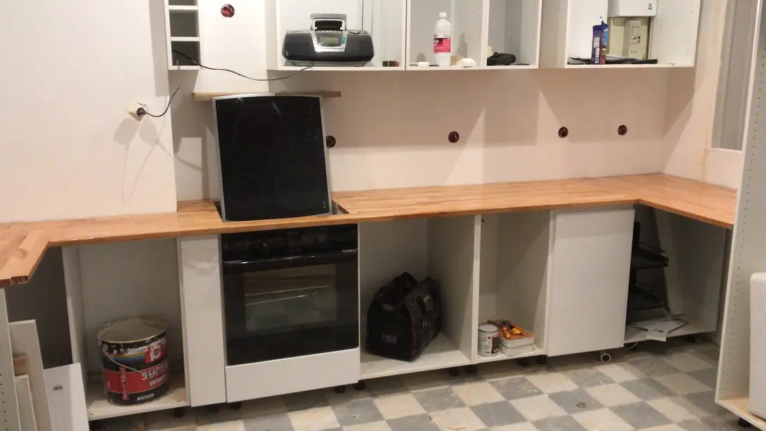 Cuisine en cours de montage : caissons blancs, plan de travail en bois et four encastré