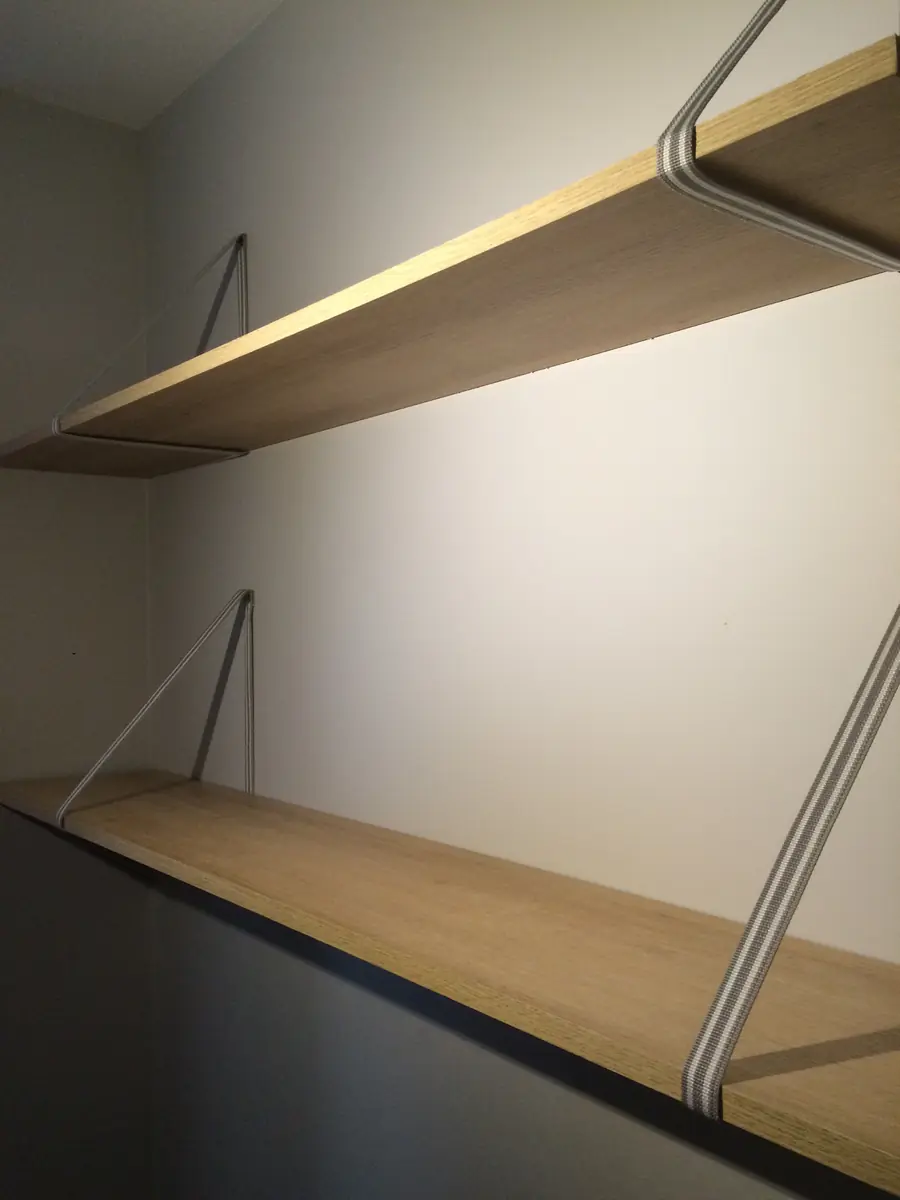 Étagères en bois clair sur mesure, fixées au mur avec des équerres métalliques