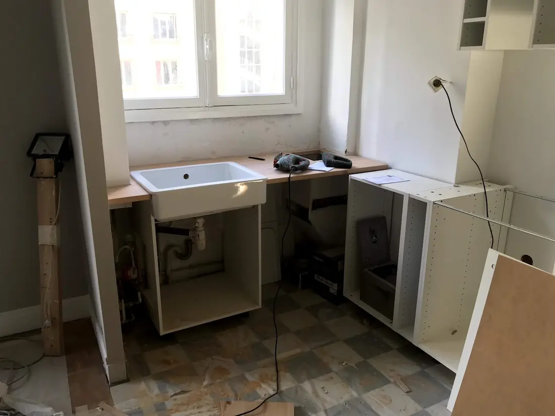 Montage d’une cuisine en cours : caisson d’évier et meubles bas ouverts sur le chantier