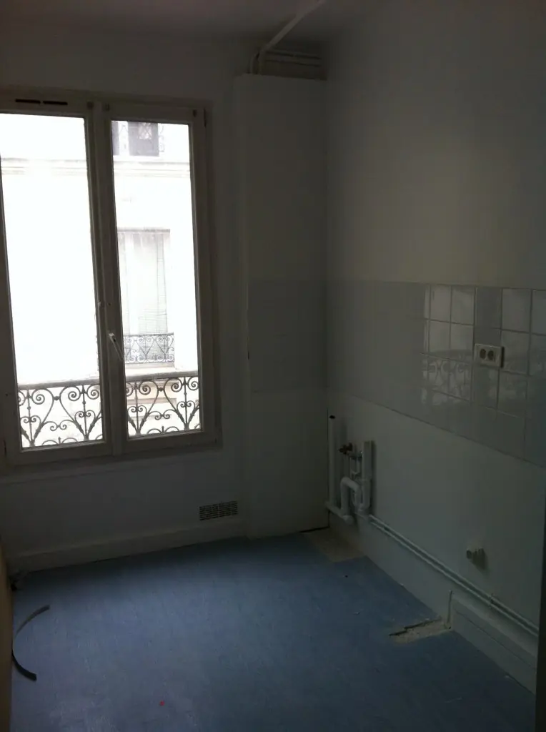 Cuisine parisienne avant le montage : pièce vide, faïence blanche et fenêtre sur cour