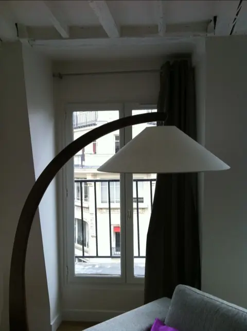 Fenêtre d’un appartement parisien équipée d’une tringle et d’un rideau, avec lampadaire