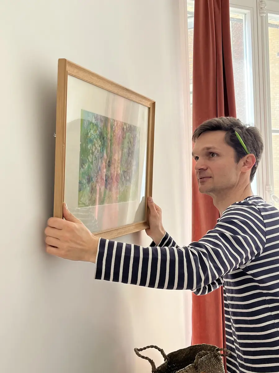 Quentin accroche un grand cadre au mur d’un salon à Paris