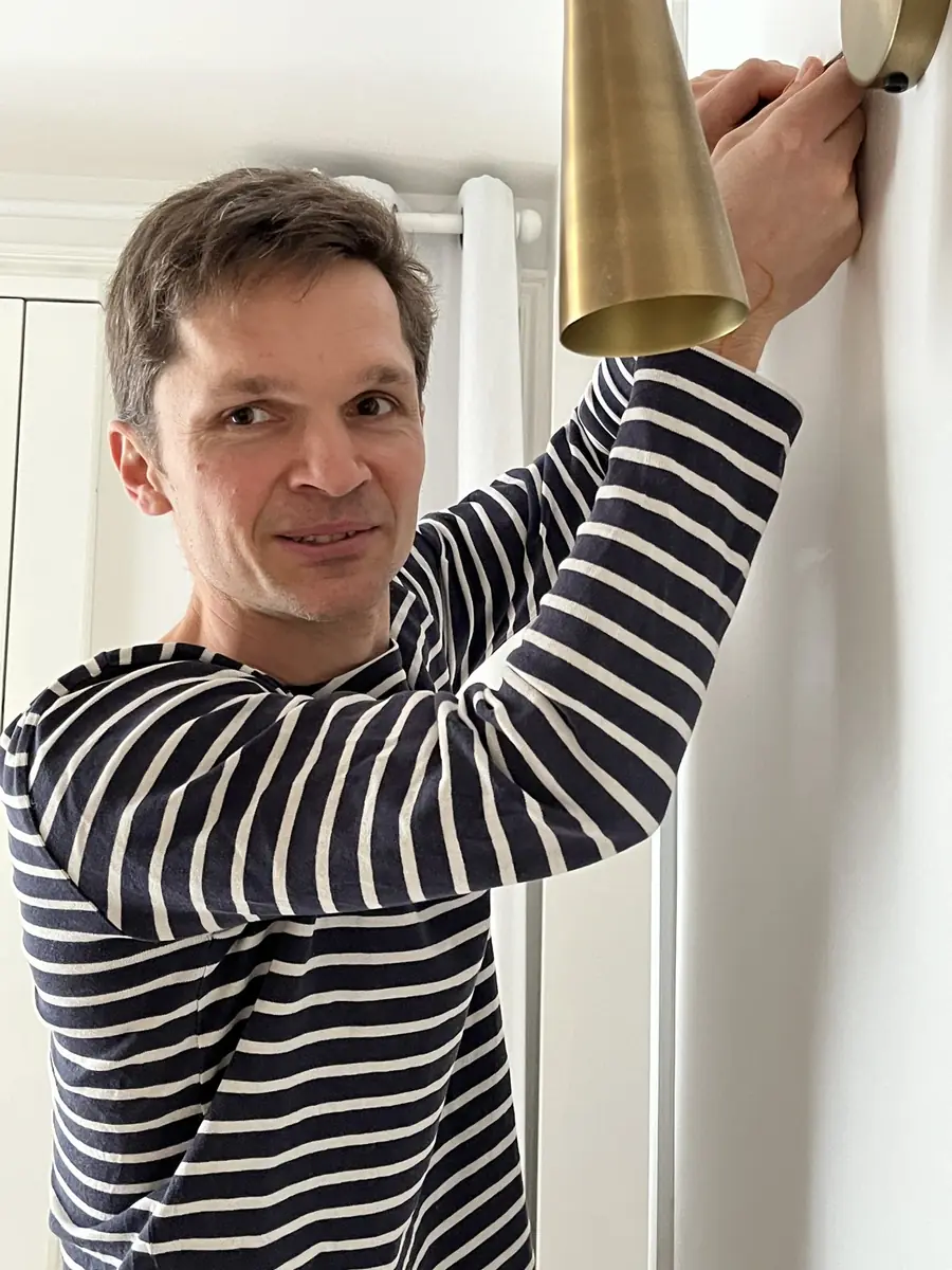 Quentin fixe une applique murale en laiton et sourit à l’objectif