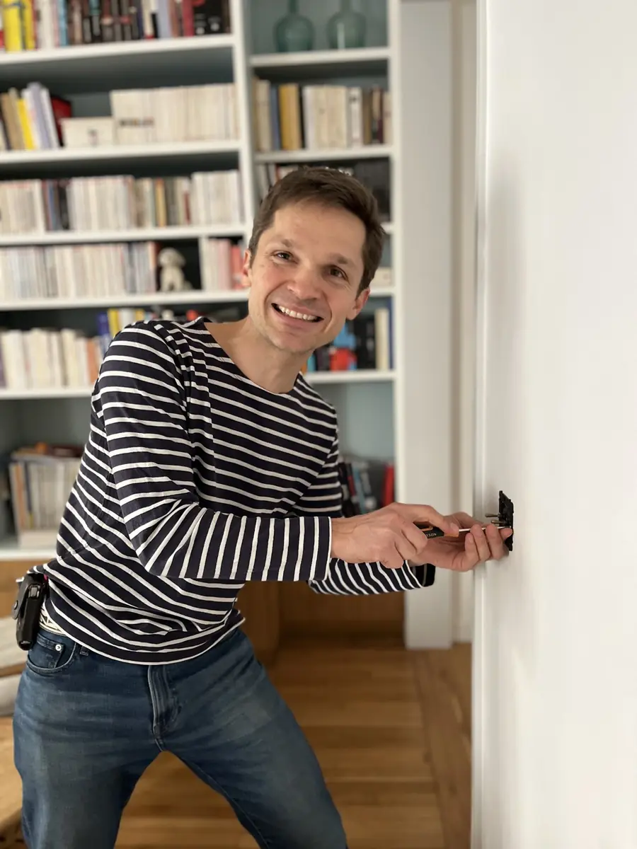 Quentin remplace une prise électrique dans un séjour avec bibliothèque