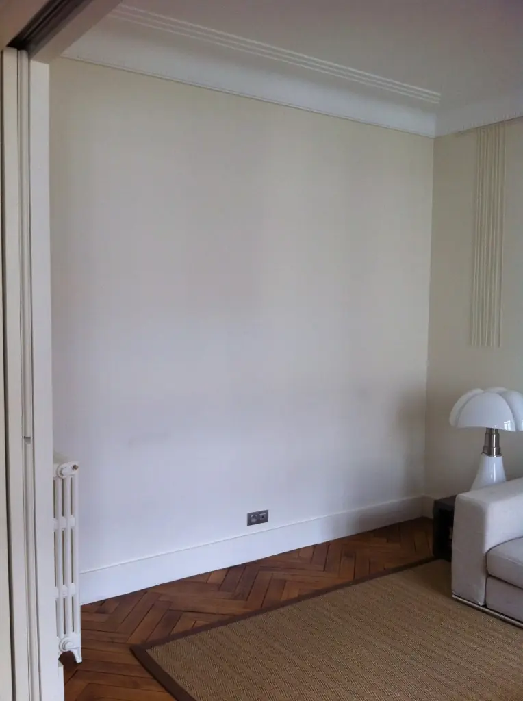 Salon parisien : mur blanc fraîchement peint, parquet et radiateur